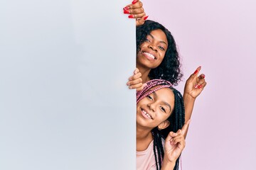 Beautiful african american mother and daughter holding blank empty banner smiling happy pointing with hand and finger to the side