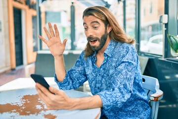 Young middle eastern man doing video call using smartphone at coffee shop.