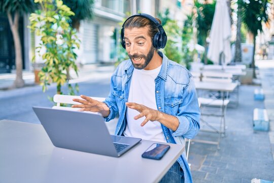 Young middle eastern man doing video call using laptop and headphones at coffee shop terrace.