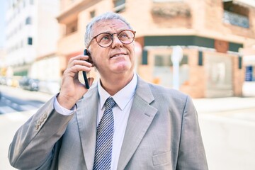 Senior grey-haired businessman using smartphone walking at street of city