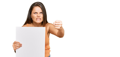 Young caucasian woman holding blank empty banner annoyed and frustrated shouting with anger, yelling crazy with anger and hand raised