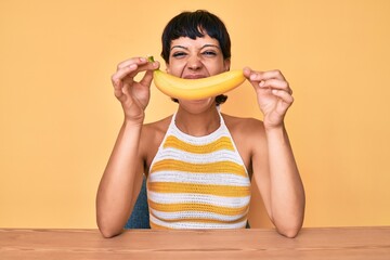 Brunette teenager girl holding banana like funny smile smiling and laughing hard out loud because...