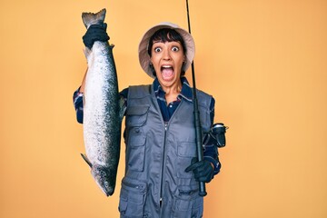 Beautiful brunettte fisher woman holding fishing rod and raw salmon celebrating crazy and amazed...