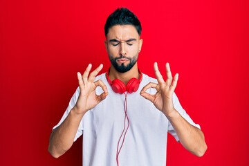 Young man with beard listening to music using headphones relaxed and smiling with eyes closed doing meditation gesture with fingers. yoga concept.