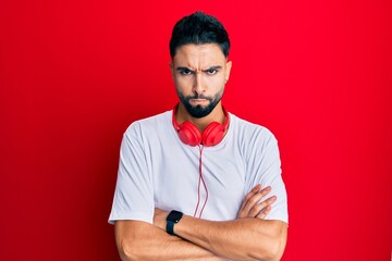 Young man with beard listening to music using headphones skeptic and nervous, disapproving...