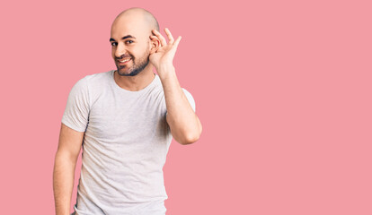 Young handsome man wearing casual t shirt smiling with hand over ear listening an hearing to rumor or gossip. deafness concept.