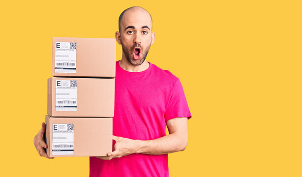 Young handsome man holding delivery package scared and amazed with open mouth for surprise, disbelief face