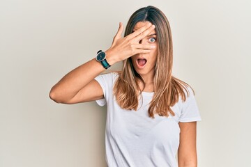 Fototapeta premium Brunette young woman wearing casual white t shirt peeking in shock covering face and eyes with hand, looking through fingers afraid