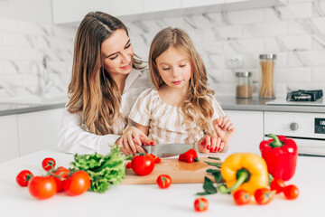 Mother with her daughter having fun and cooking salad in kitchen at home. Happy family.