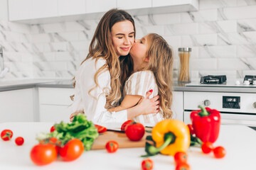 Mother with her daughter having fun and cooking salad in kitchen at home. Happy family.
