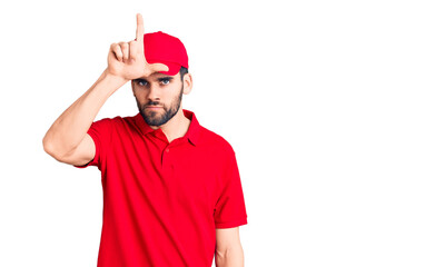 Young handsome man with beard wearing delivery uniform making fun of people with fingers on forehead doing loser gesture mocking and insulting.