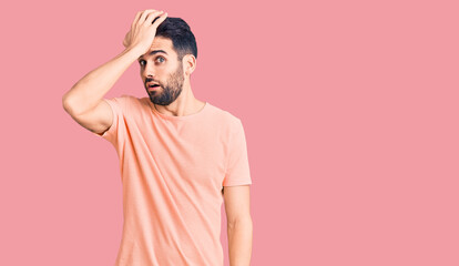 Young handsome man with beard wearing casual t-shirt surprised with hand on head for mistake, remember error. forgot, bad memory concept.