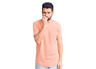 Young handsome man with beard wearing casual t-shirt looking stressed and nervous with hands on mouth biting nails. anxiety problem.