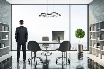 Businessman looking to window in modern coworking office with computers