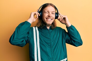Handsome caucasian man with long hair wearing gym clothes and using headphones winking looking at...