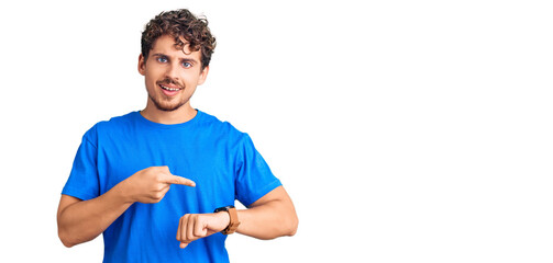 Young handsome man with curly hair wearing casual clothes in hurry pointing to watch time,...