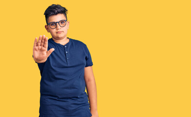 Little boy kid wearing casual clothes and glasses doing stop sing with palm of the hand. warning...