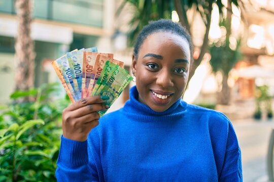 Young african american woman smiling happy holding south african rands banknotes at the park.