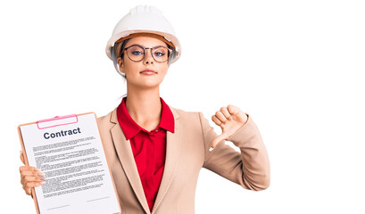 Young beautiful woman wearing architect hardhat holding clipboard with contract document with angry face, negative sign showing dislike with thumbs down, rejection concept