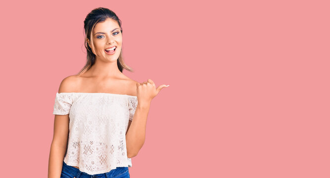 Young beautiful woman wearing casual clothes smiling with happy face looking and pointing to the side with thumb up.