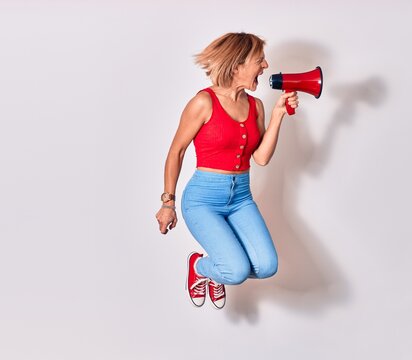 Young beautiful caucasian woman screaming using megaphone. Jumping over isolated white background