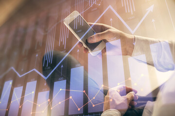 Double exposure of man's hands holding and using a digital device and forex graph drawing. Financial market concept.