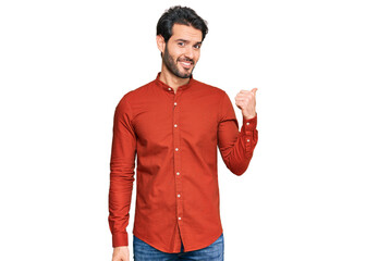 Young hispanic man wearing casual clothes smiling with happy face looking and pointing to the side with thumb up.