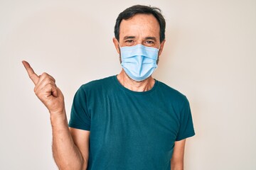 Middle age hispanic man wearing medical mask smiling happy pointing with hand and finger to the side