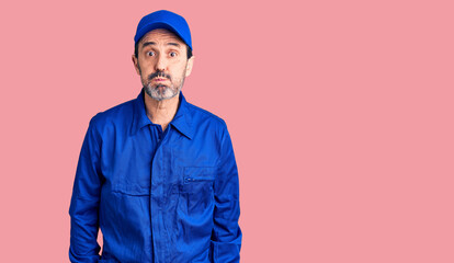 Middle age handsome man wearing mechanic uniform puffing cheeks with funny face. mouth inflated with air, crazy expression.