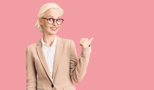 Young blonde woman wearing business clothes and glasses smiling with happy face looking and pointing to the side with thumb up.