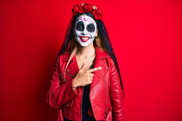 Woman wearing day of the dead costume over red cheerful with a smile of face pointing with hand and finger up to the side with happy and natural expression on face