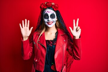 Woman wearing day of the dead costume over red showing and pointing up with fingers number eight while smiling confident and happy.