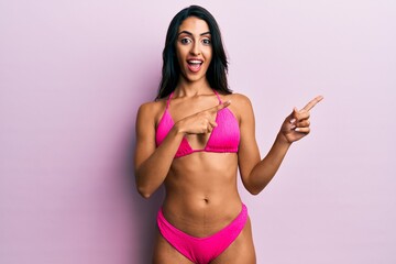 Naklejka premium Beautiful hispanic woman wearing bikini smiling and looking at the camera pointing with two hands and fingers to the side.