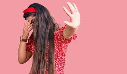 Brunette teenager girl wearing summer dress covering eyes with hands and doing stop gesture with sad and fear expression. embarrassed and negative concept.