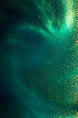 Abstract twinkling swirls of golden glitters on green background. Sparkling magic dust particles.