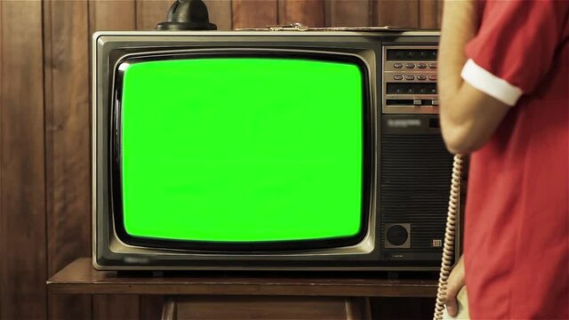 Young Man holding Old Telephone and Watching Retro TV Green Screen. You can replace green screen with the footage or picture you want with “Keying” effect in AE. 4K Resolution. 