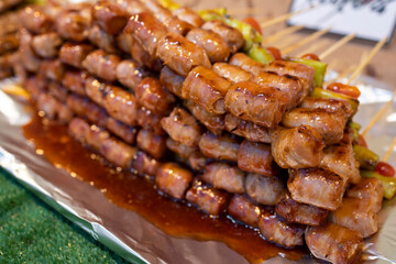 Thai street food, marinated small sausage wrapped in bacon on a skewer with a chili and tomato