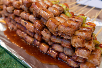 Thai street food, marinated small sausage wrapped in bacon on a skewer with a chili and tomato