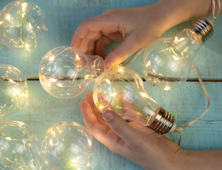 children's hand with a decorative light bulb garland on a light wooden surface