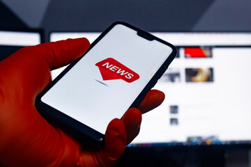 Breaking news on smartphone display. A man in medical gloves holds a phone close-up in his hand against the background of the monitor.