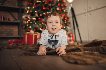 cozy Christmas card, cute preschooler lying under the Christmas tree with lights and decor in red and gold. quiet home celebration, selective focus