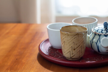 日の当たるテーブルに置かれた急須と湯気の出る温かいほうじ茶の入った湯飲み
