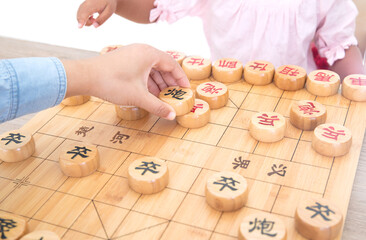 Little girl playing Chinese chess with mother