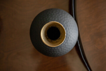 Grey ceramic vase with white interior on a wooden floor.
