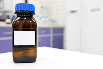 Selective focus of dark glass reagent bottle with unknown clear liquid chemical inside and blank label in a chemistry laboratory