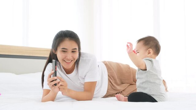 Mother using phone to play cartoon movie to make little baby happy on bed.
