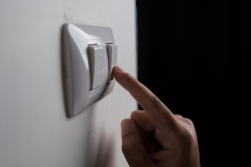 Naklejka premium Earth Hour, Close up male hand turn off the light to saving electrical energy. Finger pushing light switch turn on or off. White switch with copy space at home.