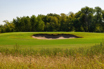 Sand trap on a golf course with trees in background