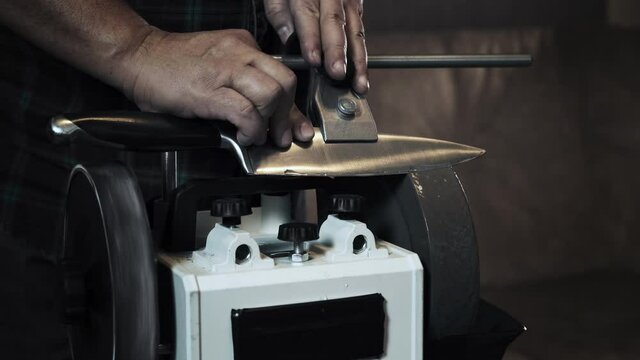 Man sharpens knives on a grinder. Close up hand