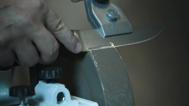 Man sharpens knives on a grinder. Close up hand